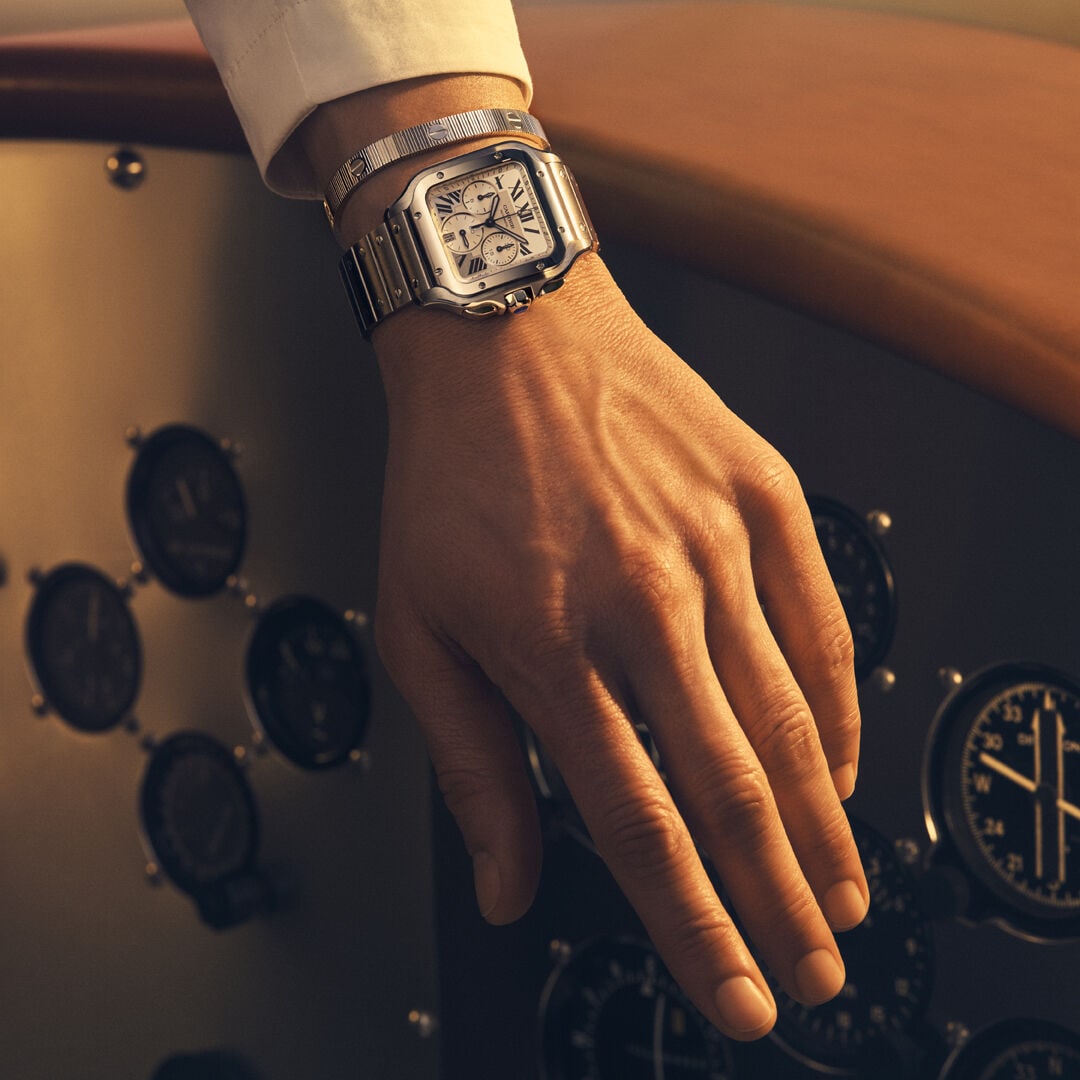 Orologio cronografo Santos de Cartier al polso, fotografato davanti agli strumenti di un aereo